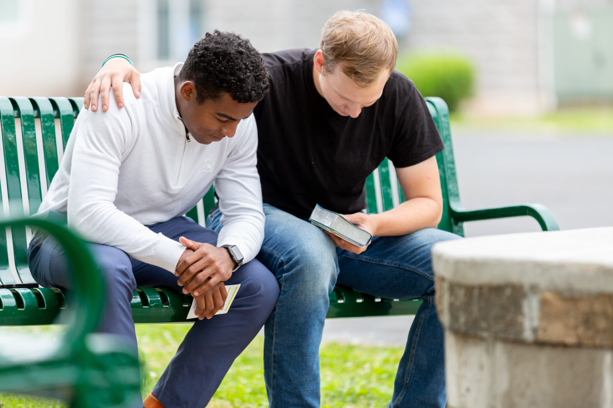 Two men praying on a park bench.